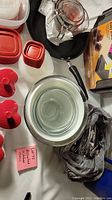 Photo showing Rubbermaid containers with red lids, a non-stick frying pan, clear glass bowls, a glass measuring cup with red markings, and a black handle frying pan, along with a bag-style milk jug and cutlery in a black bag.