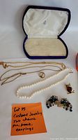 Full lot shown in case including two gold-tone chains, pearl necklace, owl brooch, decorative earrings, and snail brooch.