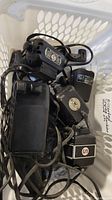 Image showing a collection of six small vintage sewing machine motors, assorted cords, and foot pedals inside a plastic basket. Items are tangled together and appear used.