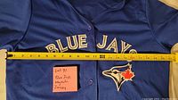 Blue Jays jersey laid flat with measuring tape showing width over chest approximately 20 inches.