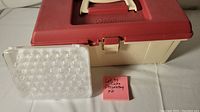 Closed Wilton cake decorating kit plastic case with red handle and latch, small plastic cookie cutters in clear plastic tray next to it.