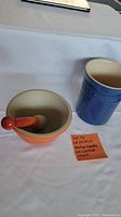 Photo of orange mortar and pestle along with the blue Le Creuset utensil crock on a white surface