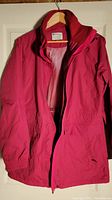 Front view of red Mountain Warehouse wind and rain coat on hanger showing zipper closure and general condition.
