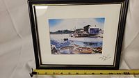Framed watercolour painting showing a coastal harbor scene with boats and buildings, tape measure indicating roughly 9" height