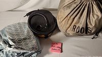 Inflatable mattress storage bag labeled Roots, foot air pump, and folded sheets on white surface
