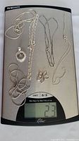 All five silver chains and assorted silver pendants placed on a digital scale showing total weight of 23 grams.