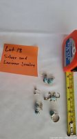 Full lot including two pairs of silver and Larimar earrings, silver Larimar lizard pendant, silver Larimar ring, and blue stone silver studs alongside measuring tape for scale.