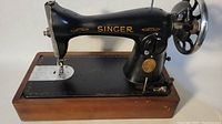 Front angle showing the whole black metal body of Singer sewing machine mounted on a wooden base.