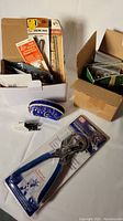 Photo of boxed vintage Singer sewing machine accessories including measuring tapes, packaged hole punch pliers with blue handles, and small sewing parts.