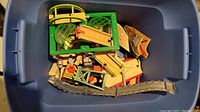Blue plastic tote filled with assorted plastic and wooden Thomas the Train track sections, bridges, and accessories seen from top down.