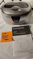 Front view of the Magnasonic ultrasonic cleaner with lid closed, manual laid in front revealing model and product name.