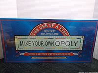 Front of the box showing title 'Make Your Own Opoly - Custom Make Your Very Own Board Game' with additional text about creating the game using pen, scissors or computer.