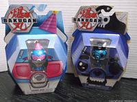 Front view of two Bakugan Cubbo figures in original packaging; one with party hat, the other pirate hat.