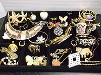 Overview of the jewelry lot arranged in a black display tray showing multiple pieces including brooches, pendants, necklaces, rings, and bracelets with varied designs such as butterflies, hearts, stars, and animal motifs.