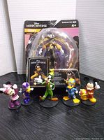 Original packaged Disney Mirrorverse Goofy figure plus five assorted Disney character figurines lined up in front of packaging, including Minnie Mouse, Daisy Duck, Goofy, Donald Duck, and Mickey Mouse.