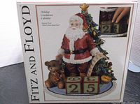 Decorative ceramic figurine showing Santa Claus with a Christmas tree, teddy bear, and three numbered blocks for countdown days.