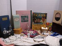 Wide view showing the entire lot with vintage jewelry, books including the TV Talk 1969 magazine, Estee Lauder cosmetic boxes, decorative glass bottles, gloves, and various personal items arranged on a white background.