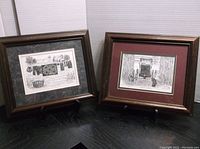 Two framed black and white prints displayed on a black surface, showing rural themes and signed numbers.