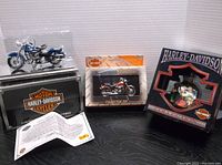 Photo showing the 1:18 scale die cast 1953 Hydra Glide model in black display case, the playing card collector tin packaging, and the ornament box together