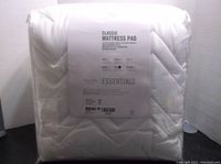 Front view of the packaged mattress pad showing label details including 'Classic Mattress Pad', 'Martha Stewart Essentials', and size information.