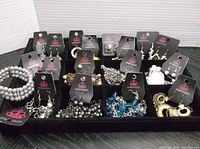 Display of 10 pairs of earrings on Paparazzi black card mounts, plus multiple necklace and earring sets and a bracelet, arranged in trays.