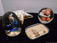 Four varied paperweights including a starfish figurine, a dark glass signed piece, a rectangular vintage style paperweight with a ship image, and a round glass piece with orange inclusions.
