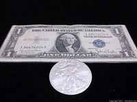 Obverse side of 1935 D one dollar silver certificate note and front view of 2011 Silver Eagle coin showing Walking Liberty design.
