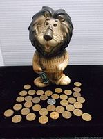 Full view of Vintage Lefton lion ceramic bank with around fifty wheat pennies and one quarter arranged in front on a black surface.