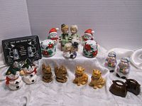 Eleven salt and pepper shaker sets displayed together including holiday, animal, and figurine styles on white fabric background.