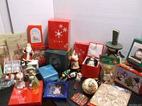 Wide view of the lot showing multiple Christmas-themed items from various brands including figurines, ornaments in boxes, and holiday tins arranged closely together.