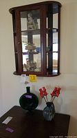Wall hanging curio cabinet displaying ceramic figurines, two vases on table below