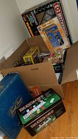Boxes and items including Texas Hold'em Poker set, Trivial Pursuit, puzzles, and remote control truck packed in cardboard boxes.