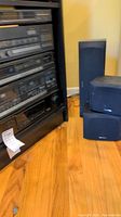 Photo showing three Kenwood speakers (one tall floor-standing and two smaller) placed near the AV receiver rack