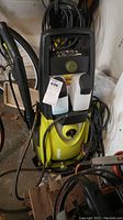 Front view of the green and black Sun Joe SPX3000 electric power washer with attached hoses and power cord, showing the two detergent bottles and control dial.