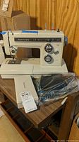 Front view of Kenmore sewing machine model 17600 sitting on a wooden table with instruction manual and accessories in plastic bags placed beside it.