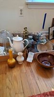 Full lot view showing various vases, teapot, bowls, bells, and music box decor on wooden floor