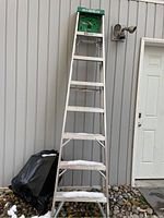Full length photo of the aluminum step ladder showing the 8 ft height and overall structure against a beige siding wall.