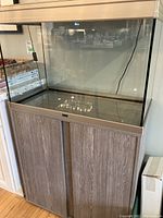 Front view of glass aquarium with aluminum frame and sliding hood on matching wood-grain cabinet stand