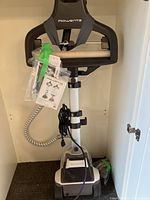 Full view of Rowenta clothes steamer unit including hanger, steam hose, power cord, and base with wheels placed inside a closet.