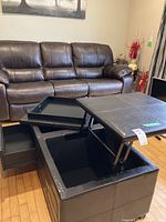 Coffee table with top raised showing large interior storage compartment lined with black material.