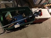 Wide shot showing fishing rods with reels inside green toolbox, two handheld ice augers resting on top of coolers, several coolers stacked beside each other