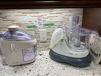 Two kitchen appliances on counter: Hamilton Beach juice extractor on left and T-Fal Kaleo food processor on right with manuals visible.