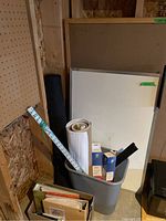 Photo showing white bulletin board, white dry erase board, gray plastic waste can filled with rolled papers and binders, standing in wood-paneled room.