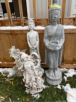 Four garden statues grouped outdoors against wooden fence, snow on ground