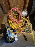 Multiple coiled extension cords in orange and yellow colors with packed hardware items in a plastic bin