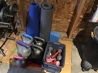 Overview photo showing kettlebells, yoga mats, dumbbells, and foam block organized on floor.