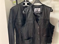 Both black leather vest and jacket hanging on hangers