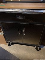 Front view showing black diamond plate drawer and dual doors on caster wheels