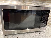 Front view of the Insignia microwave oven showing stainless steel body, glass door, and brand logo beneath door.