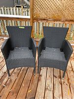 Pair of black woven patio chairs on wooden deck, front view showing both chairs side by side.